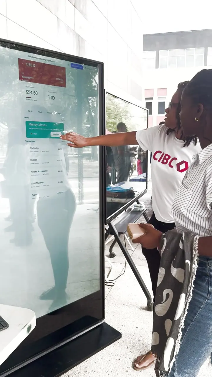 CIBC staff demonstrating their gamified youth eBanking app on a Timesquare vertical touchscreen kiosk at UWI St. Augustine