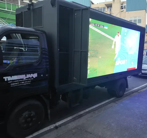 Matte black Timesquare truck in livery at the kerb on CPL 2026 match night, its side screen carrying a live football feed